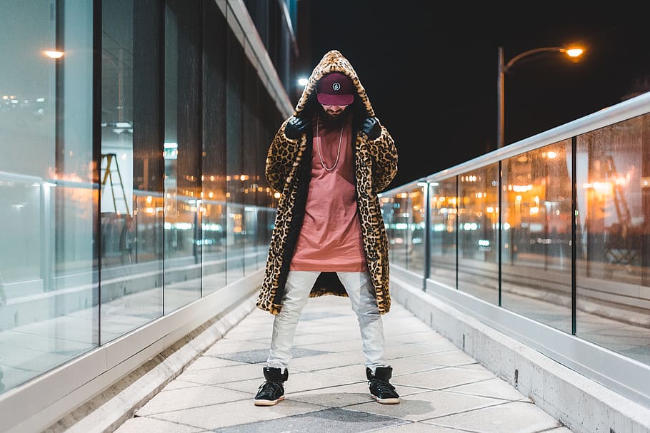 man wearing brown leopard print hooded coat, pink shirt, whit epants and black high-top sneakers beside glass building at night, HD wallpaper