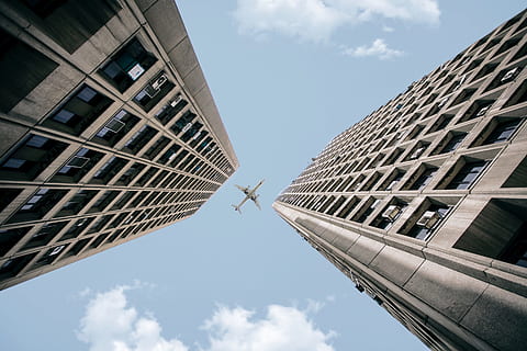 low angle photography of airplane crossing on two high rise buildings during daytime HD wallpaper