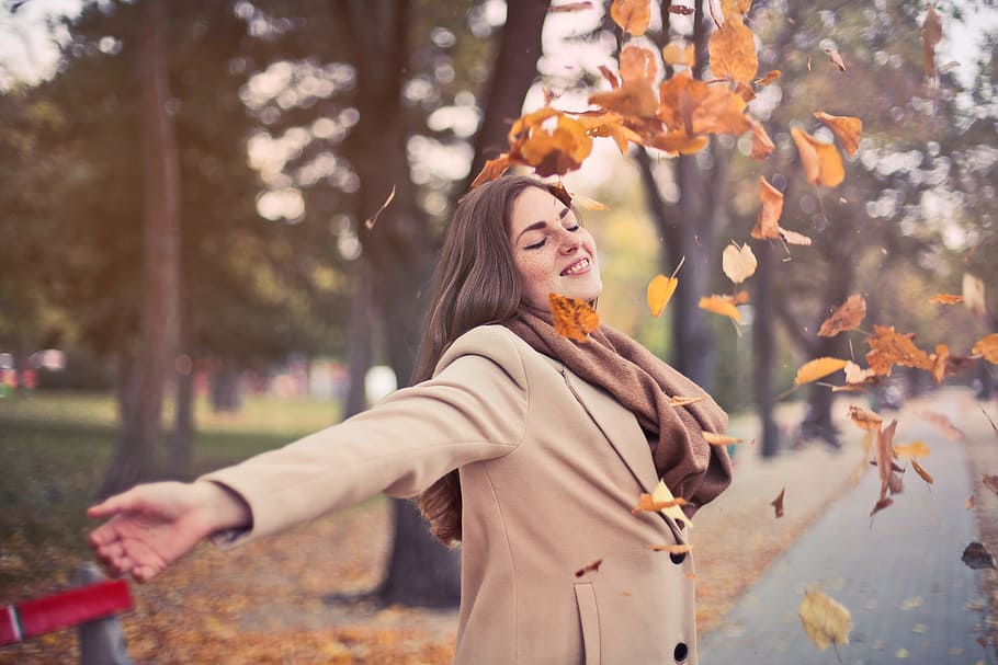 Beautiful young adult woman wearing brown scarf and camel overcoat as playing among falling autumn leaves, HD wallpaper