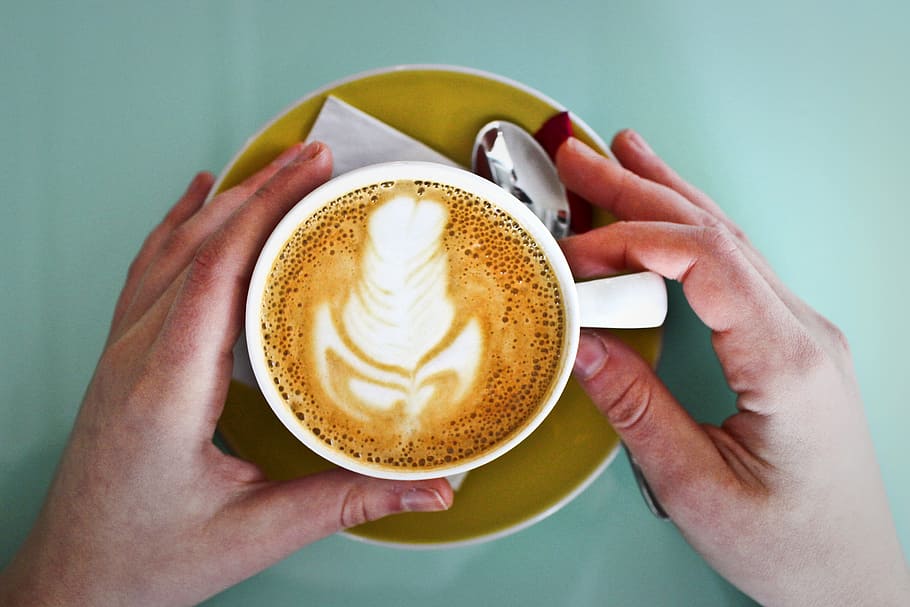 A coffee cup held by hands with a spoon and a paper napkin placed on a saucer HD wallpaper