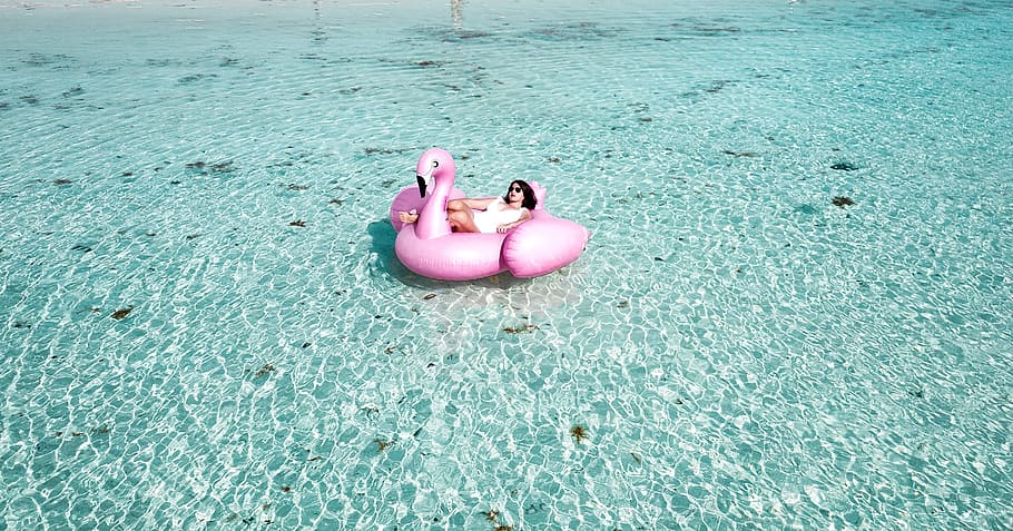 Woman Lying on Pink Flamingo Bouy on Body of Water, beach, buoy