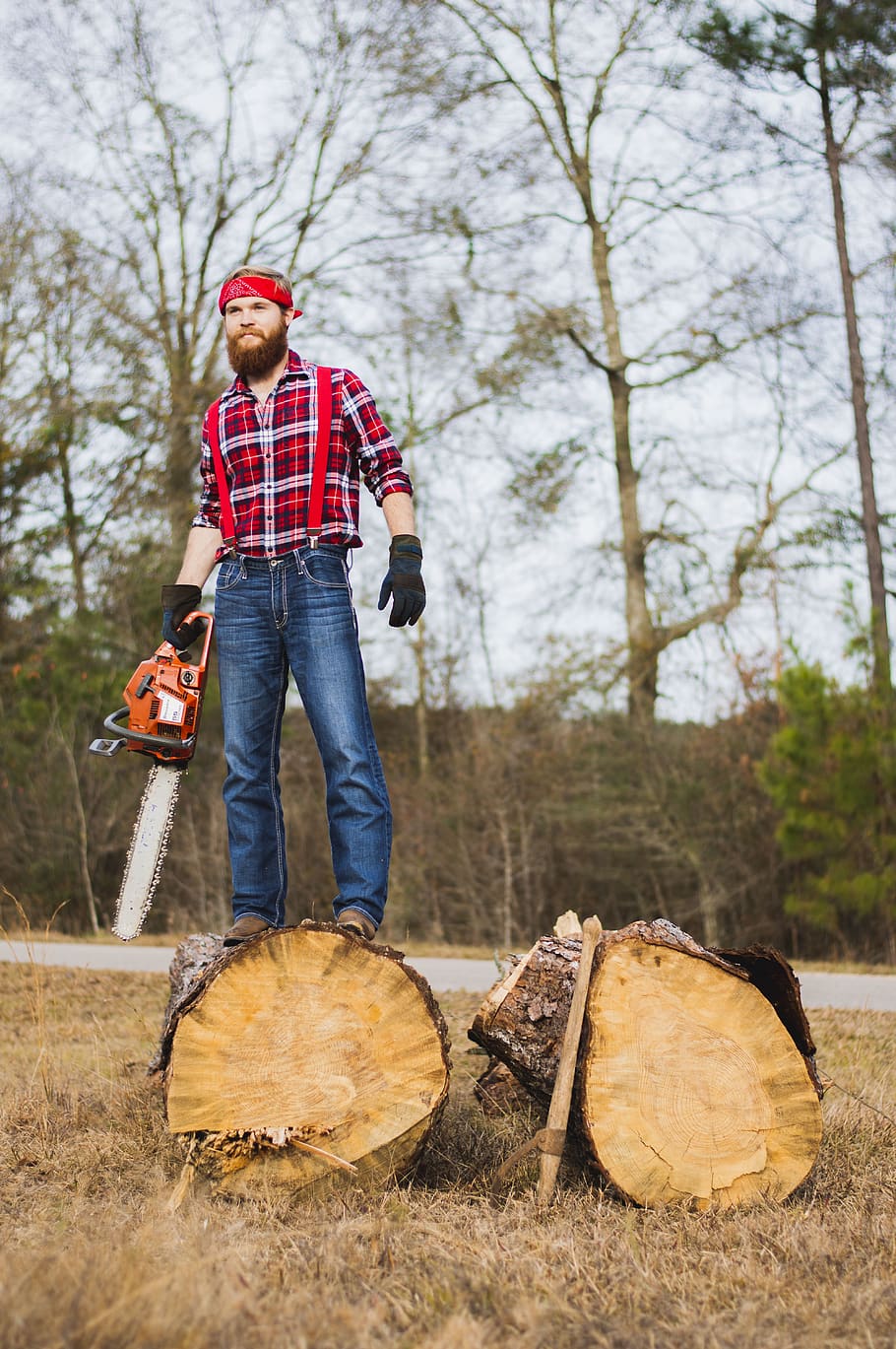 man holding chainsaw and standing on wood log, person, human