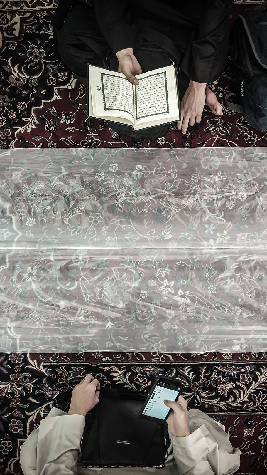 صورة اسلامية من موقع wallpaper flare Two-person-sitting-on-area-rug-one-holding-quran-and-the-other-using-smartphone