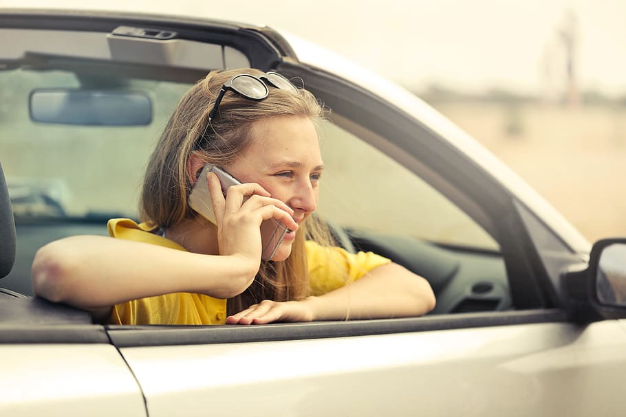 Young Woman Wearing Half-Sleeved Yellow Shirt Talking On Phone While Sitting In Her Car HD wallpaper