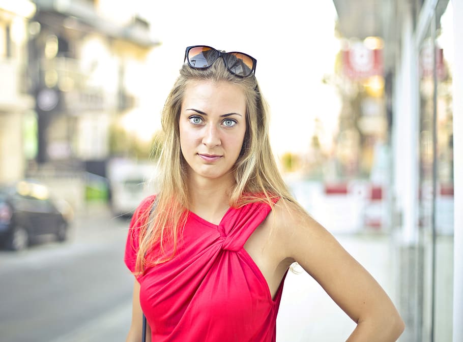 A blonde young woman wearing red dress and sun glasses posing on the side walk