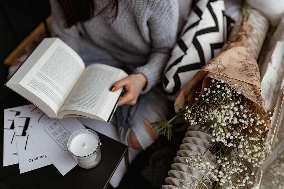 A woman in a sweater reads a book, reading, reader, opened book