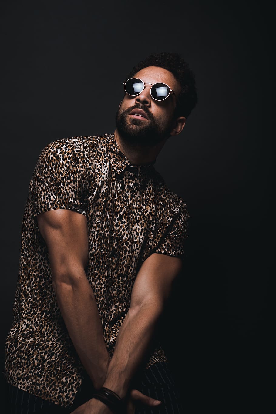 man wearing brown and black leopard print button-up T-shirt and black sunglasses crossing hands down while looking up HD wallpaper