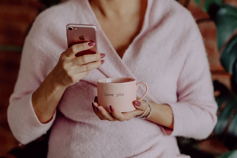 A woman in a pink sweater holds a pink iPhone and a pink cup in her hands