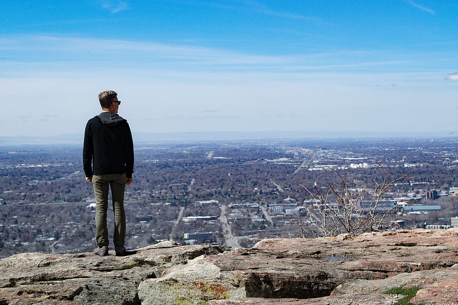 Man Wearing Black Jacket Standing on Rock Monolith, cliff, clouds HD wallpaper