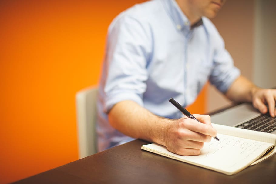Focus Photography of Person Writing on Desk Using Laptop, businessman