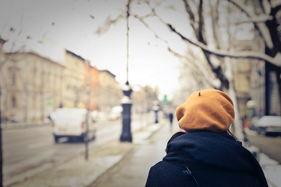 A woman wearing an orange cap walking on the sidewalk on a winter day HD wallpaper