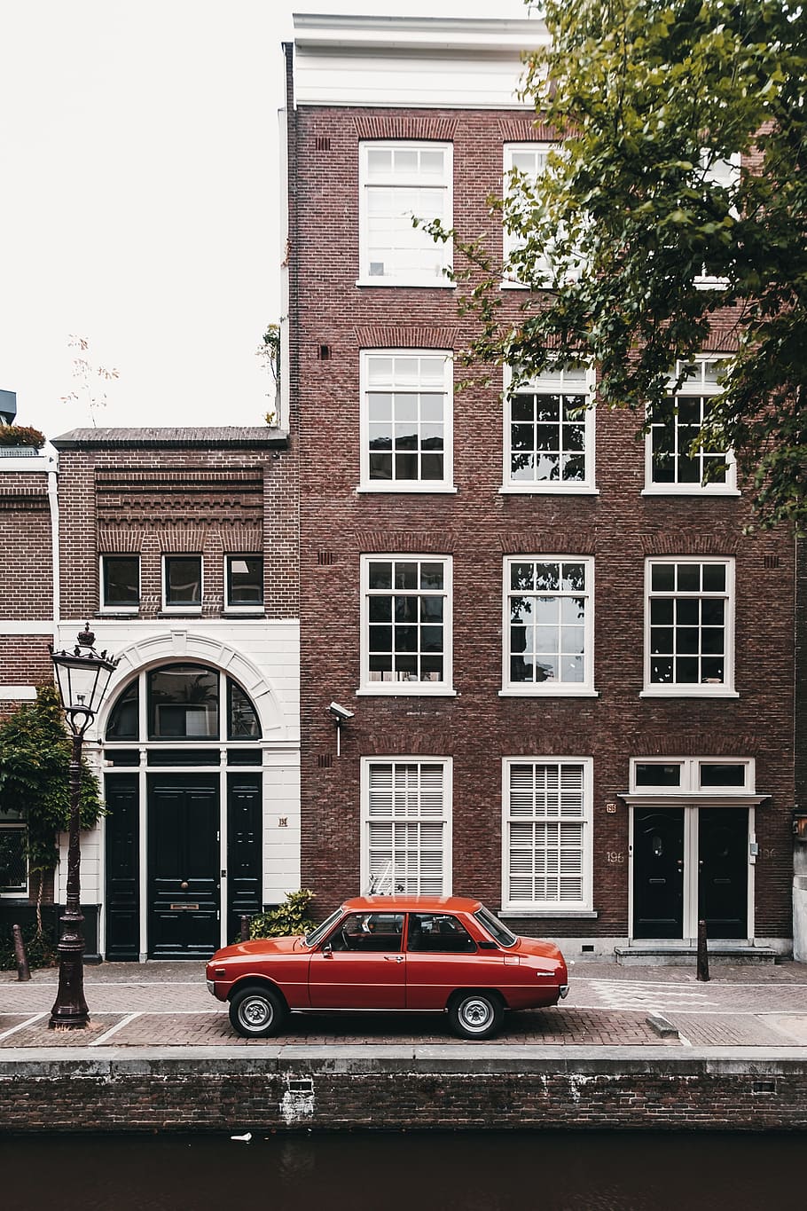 red sedan parking beside high-rise building at daytime, tree HD wallpaper