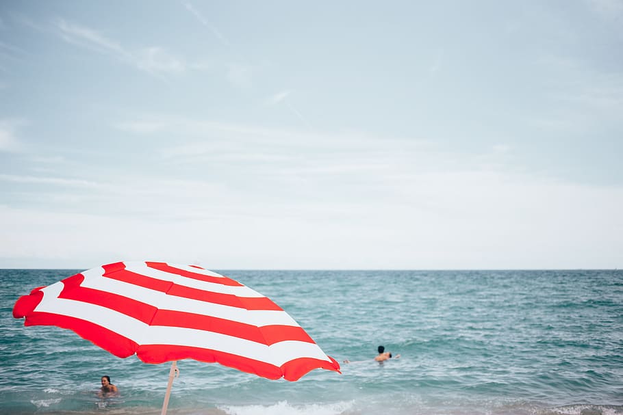 A beach umbrella with people swimming in the background, Bay HD wallpaper