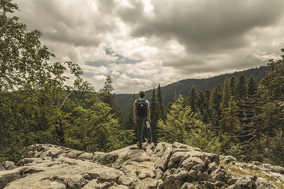 Man Standing on Cliff, adventure, backpack, clouds, conifers HD wallpaper