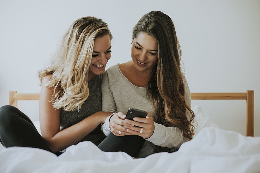 Two Women Looking at Black Smartphone, bed, bedroom, blanket