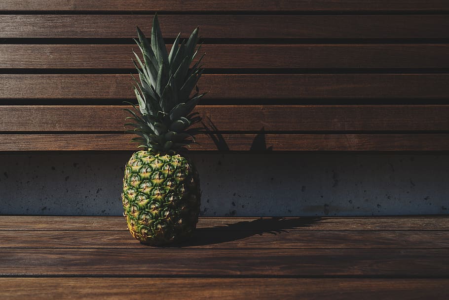 green and yellow pineapple placed on brown wooden pallet bench