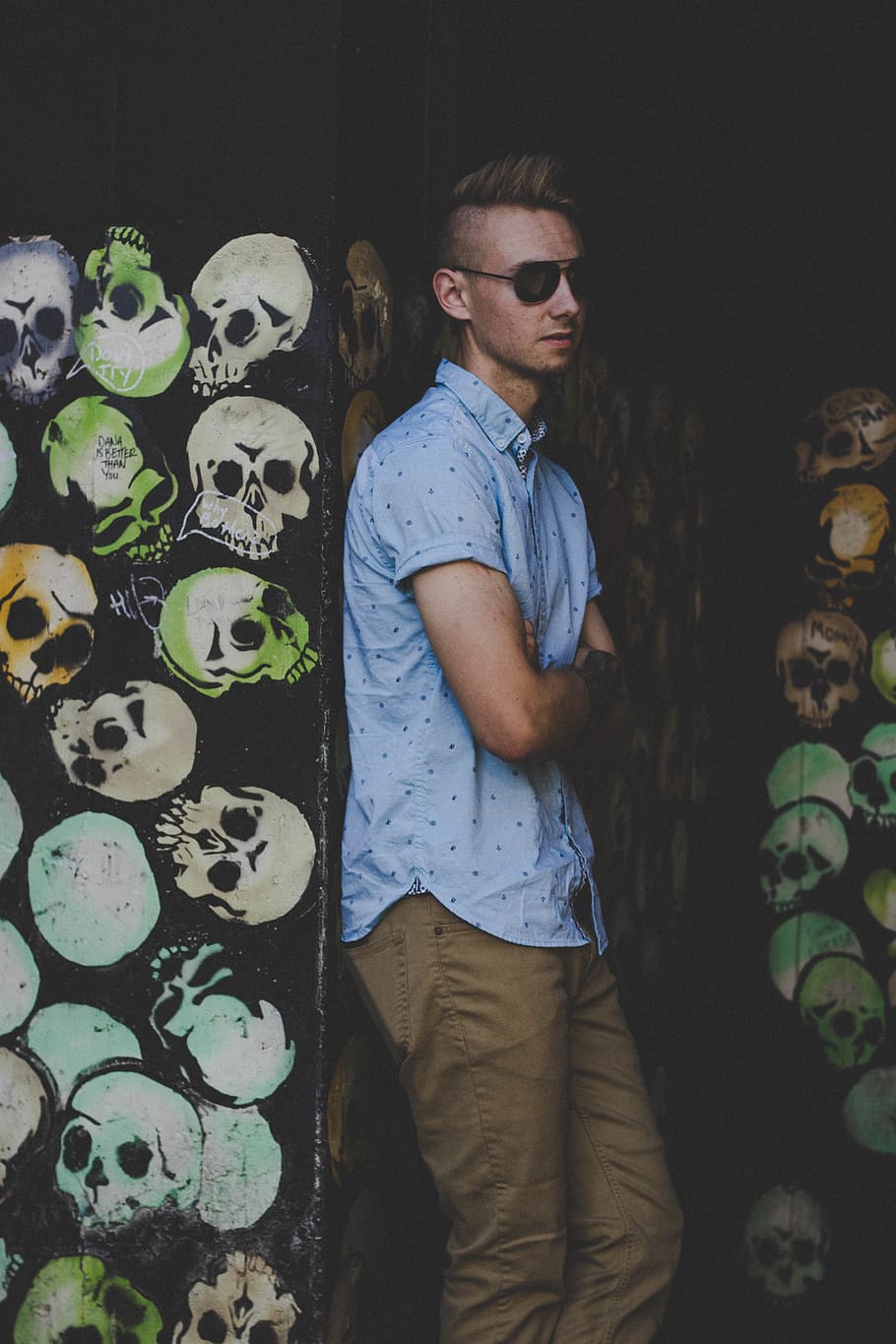 men wearing blue button-up shirt leaning on black graffitied wall