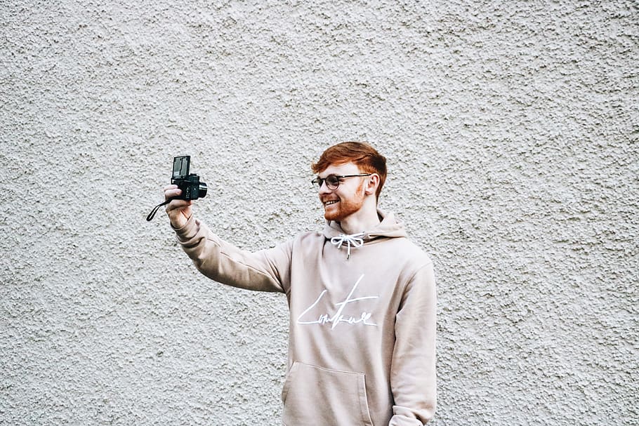 man taking selfie in front of gray wall, apparel, clothing, person