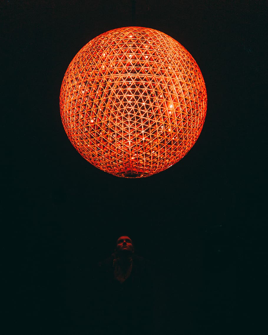 person looking at orange lighted ball on ceiling, sphere, bush