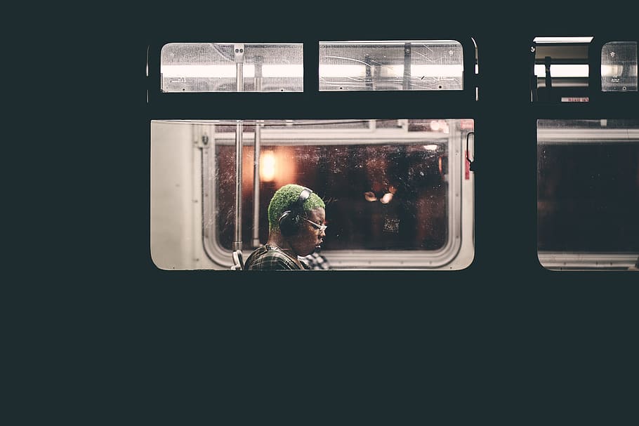 man sitting inside train wearing black headphones, night, window