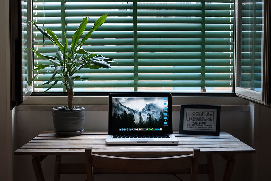 Photo of Macbook Air on a Table Next to House Plant and Picture Frame.