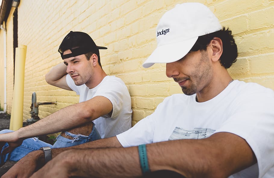 Two Men Sitting Beside Beige Concrete Wall, bricks, cap, casual HD wallpaper