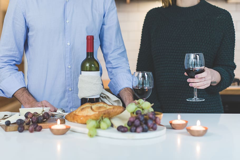 Man Standing Beside Woman Holding Wine Glass in Front of Grapes and Bread on Table HD wallpaper