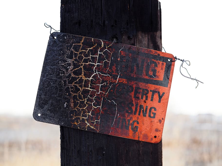 burned warning trespassing signage on post during daytime, wood