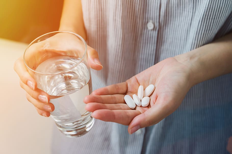 Woman arm holding heap of small round meds and glass of water before taking medication