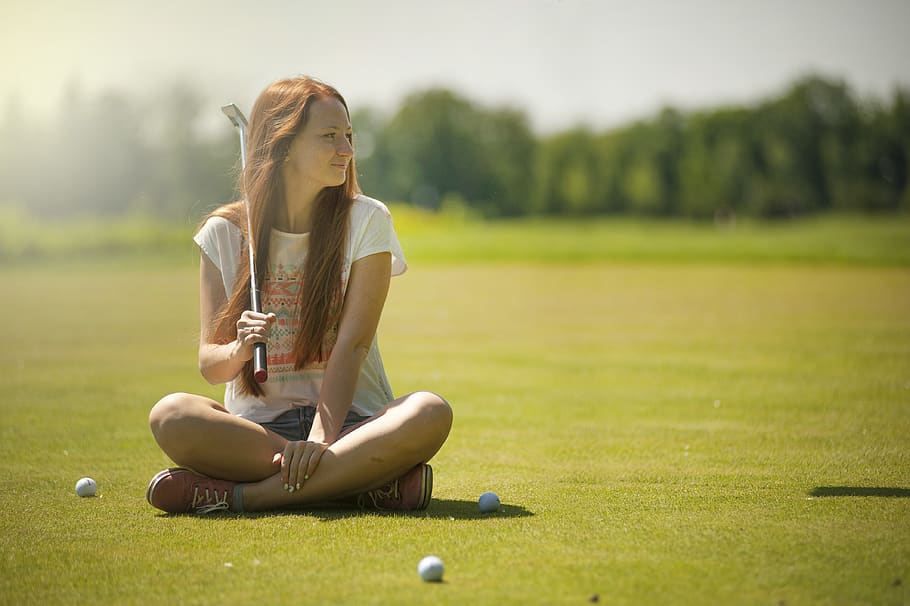 Woman in White Scoop-neck Shirt and Blue Shorts Holding a Golf Club Sitting on Golf Field
