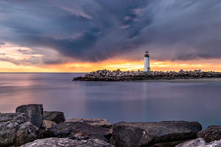white lighthouse on shore beside body of water, breakwater, sunrise