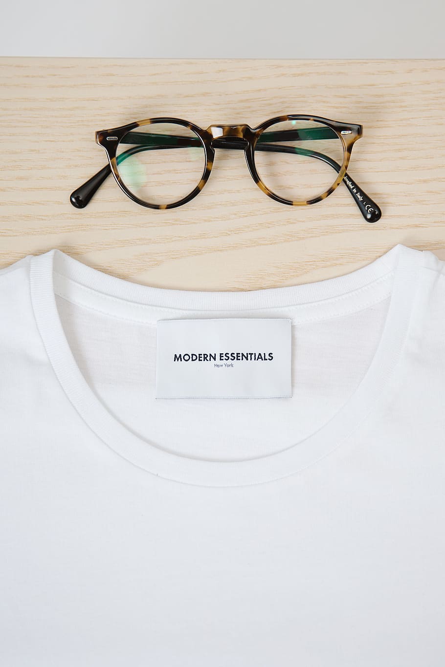 close-up photography of white Modern Essentials crew-neck shirt and black and brown framed eyeglasses on brown slab