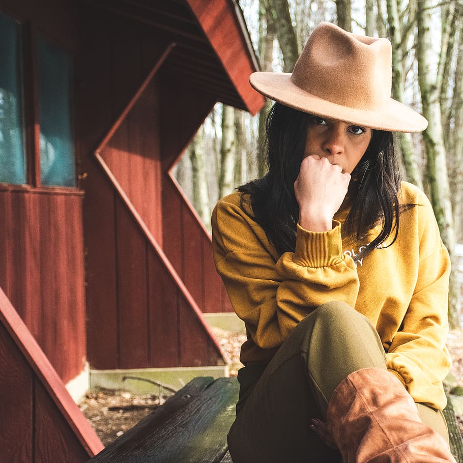 Woman in Yellow Sweater and Brown Panama Hat Sitting on Brown Wooden Table