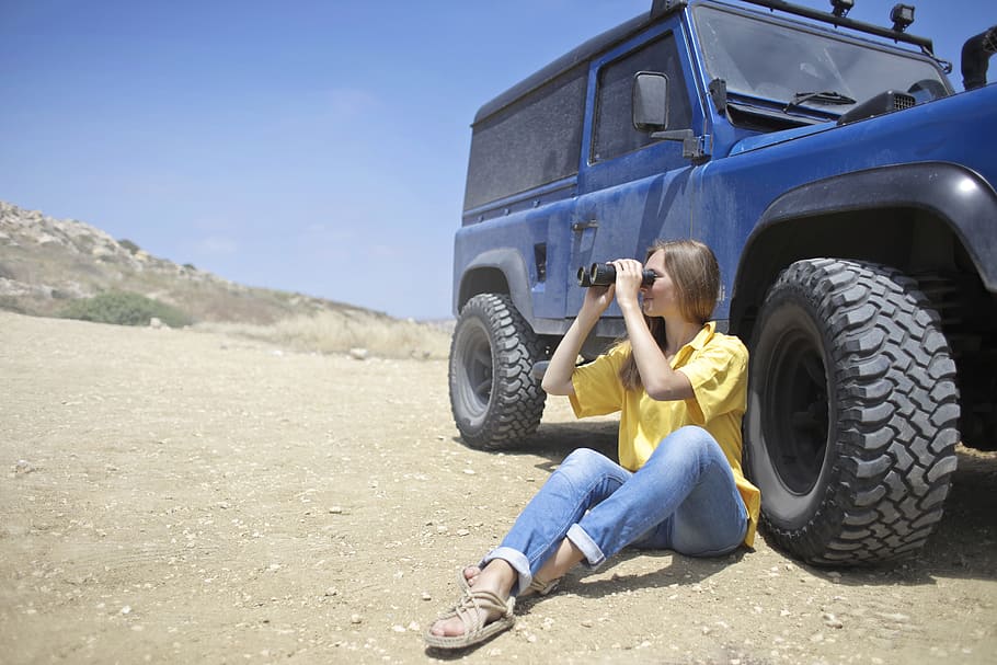 Woman Sitting on Soil Beside Jeep While Using Binoculars, adult