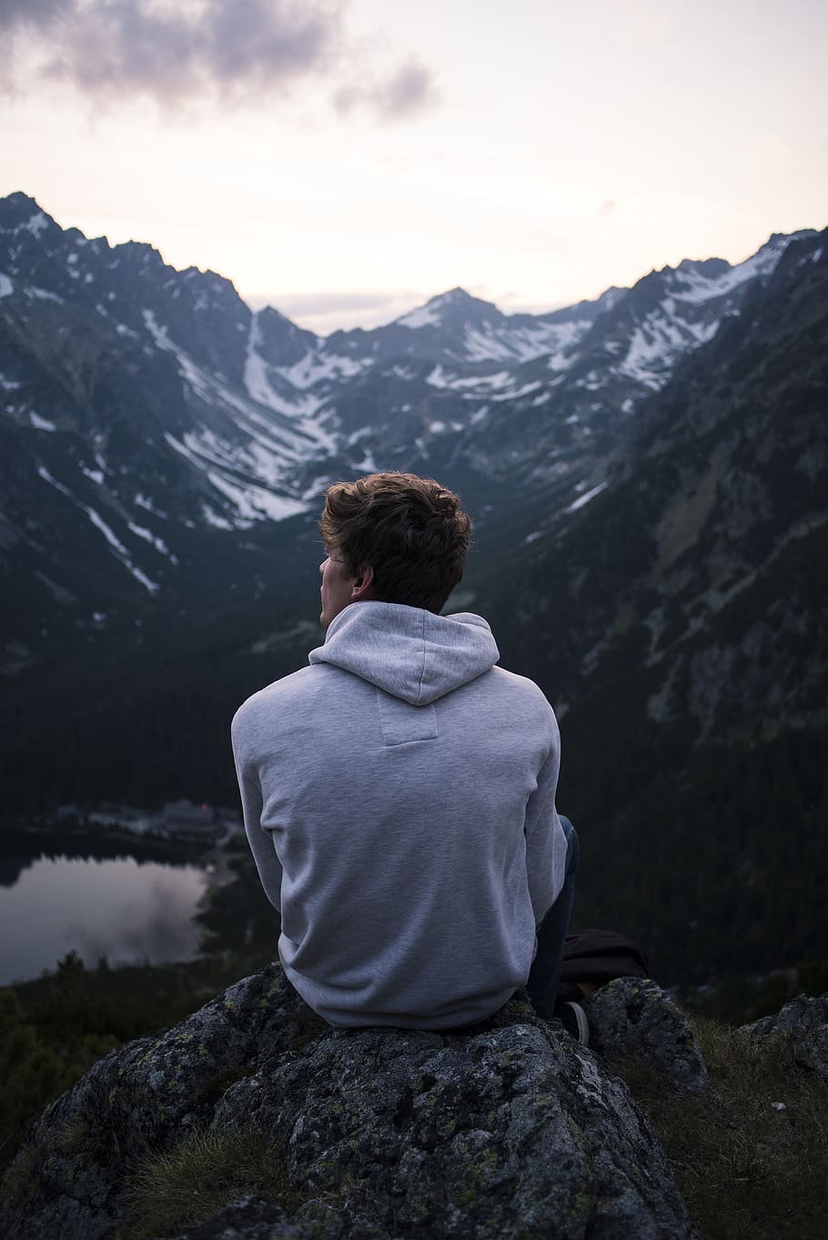 Man Wearing White Hoodie Sitting on a Rock With a View on Mountain HD wallpaper