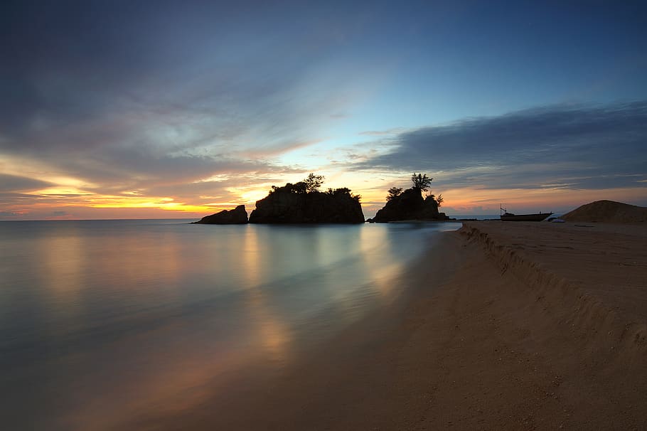 Calm Body of Water Near Shore With Silhouette of Rock Formation Against Setting Sun HD wallpaper