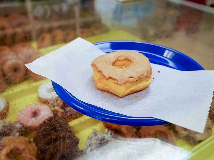 maple donut sitting on a blue plate in a donut shop., bakery