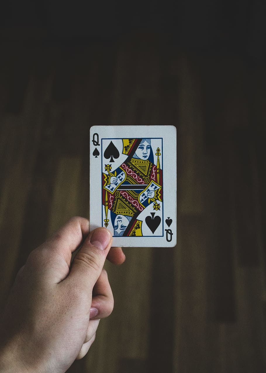 person holding Queen of spade playing card, hand, floor, wood