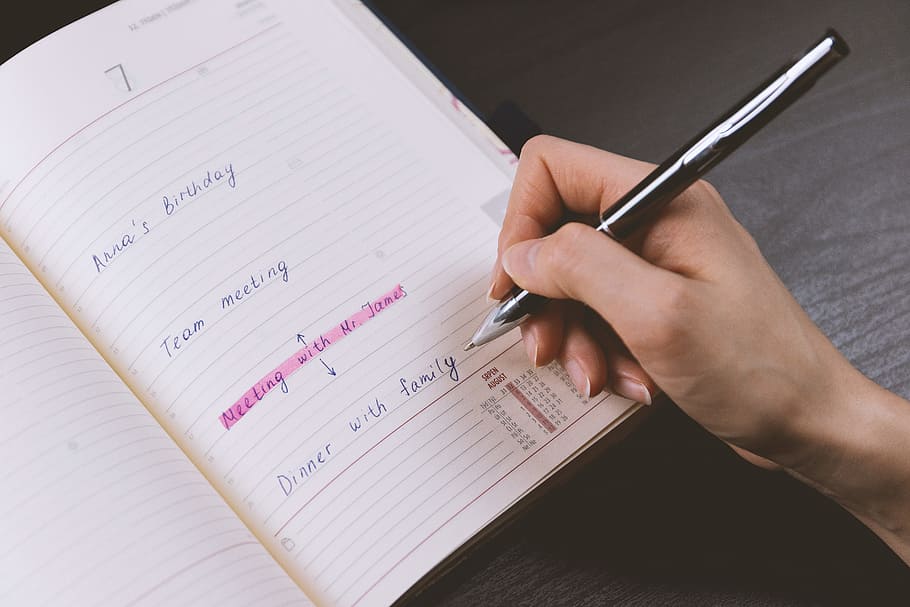 The woman’s hand holds a pencil and writes a plan into a diary at home HD wallpaper
