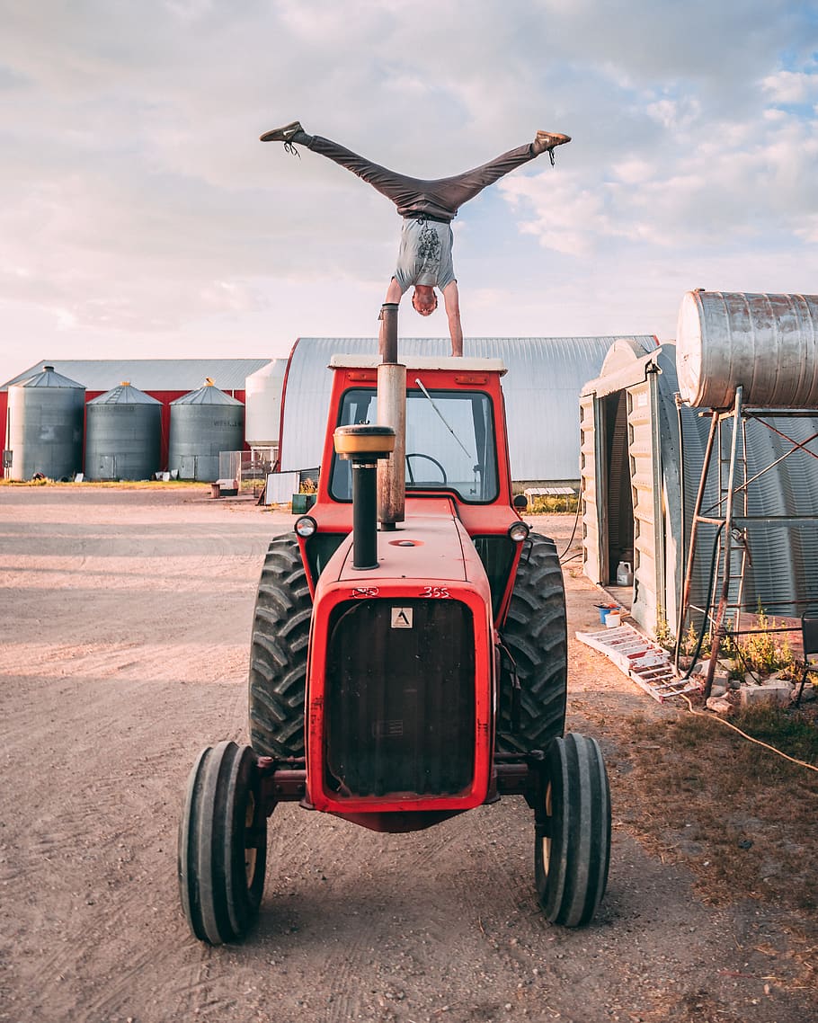man doing head stand on red tractor, machine, wheel, person, transportation HD wallpaper