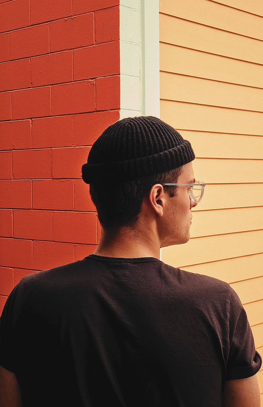A mixed race mal wearing glasses, looking to the right while standing in front of a building corner.