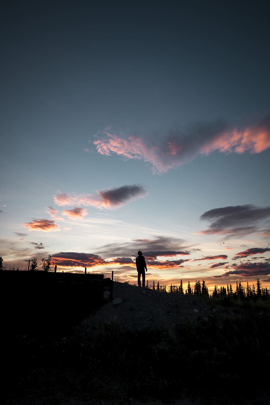 man standing on hill under gray and orange sky at golden hour HD wallpaper