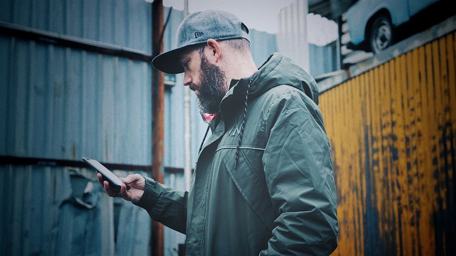 Man Wearing Black Hoodie, beard, cap, cellphone, close-up, daytime HD wallpaper