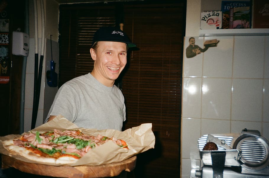 Man Standing and Smiling While Holding Pizza, chef, cooking, cuisine