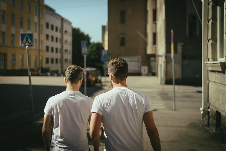 Two men in white t-shirts walk away down a city street, man, daylight