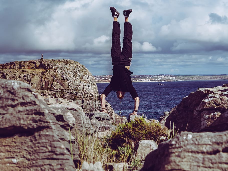 Man Wearing Black Dress Shirt and Burgundy Pants Hand Standing on Rock Formations Across Sea HD wallpaper
