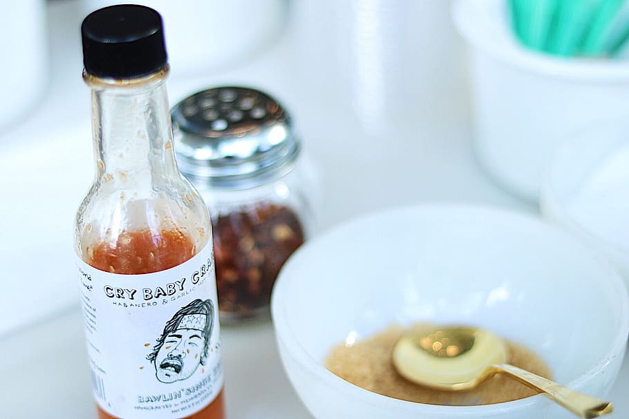 Cry Baby hot sauce beside white ceramic bowl, spoon, cutlery