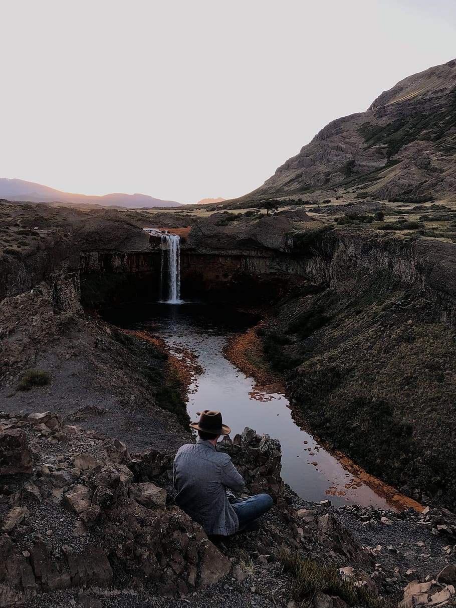 Man Sitting Near Waterfalls, cascade, mountain, nature, person HD wallpaper