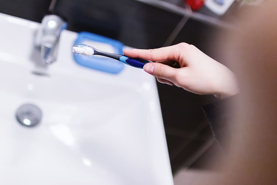 Woman hand holding toothbrush with toothpaste applied on it in bathroom HD wallpaper