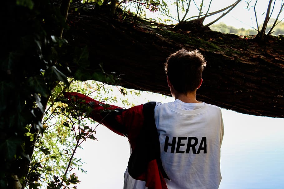 man wearing white Hera shirt standing near tree outdoors during daytime